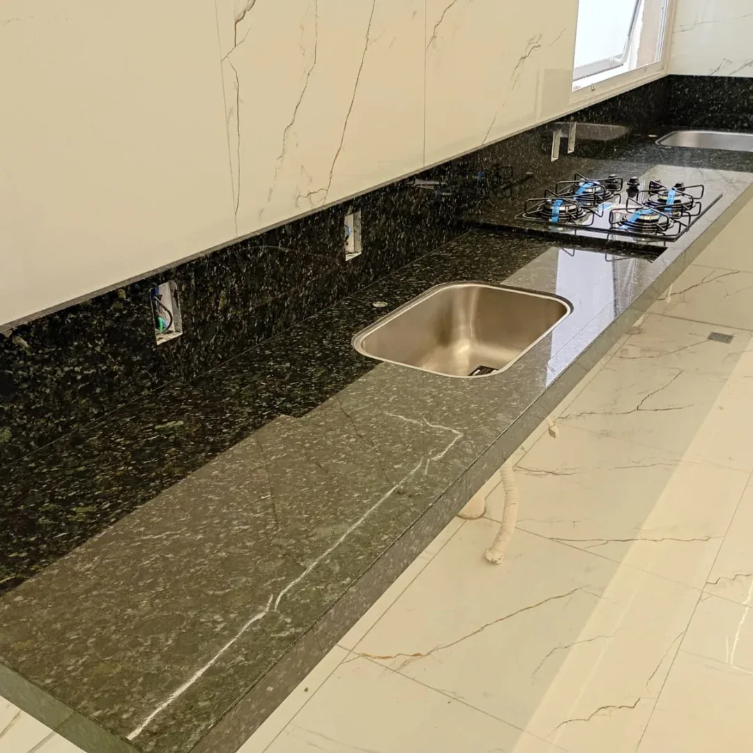 Bancada longa de granito escuro instalada com cuba inox em cozinha