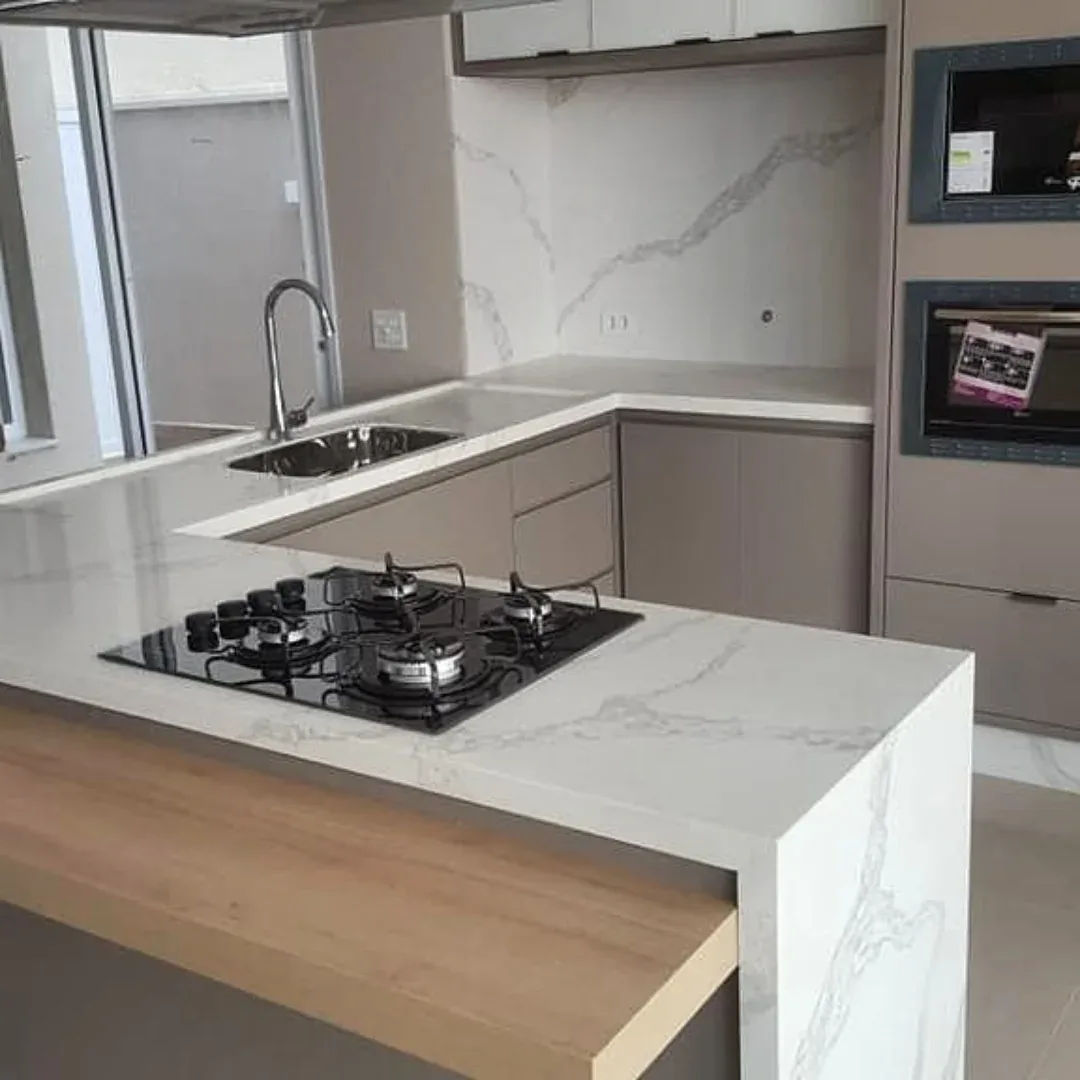 Ilha de cozinha com bancada branca de veios, cooktop embutido e prolongamento em madeira