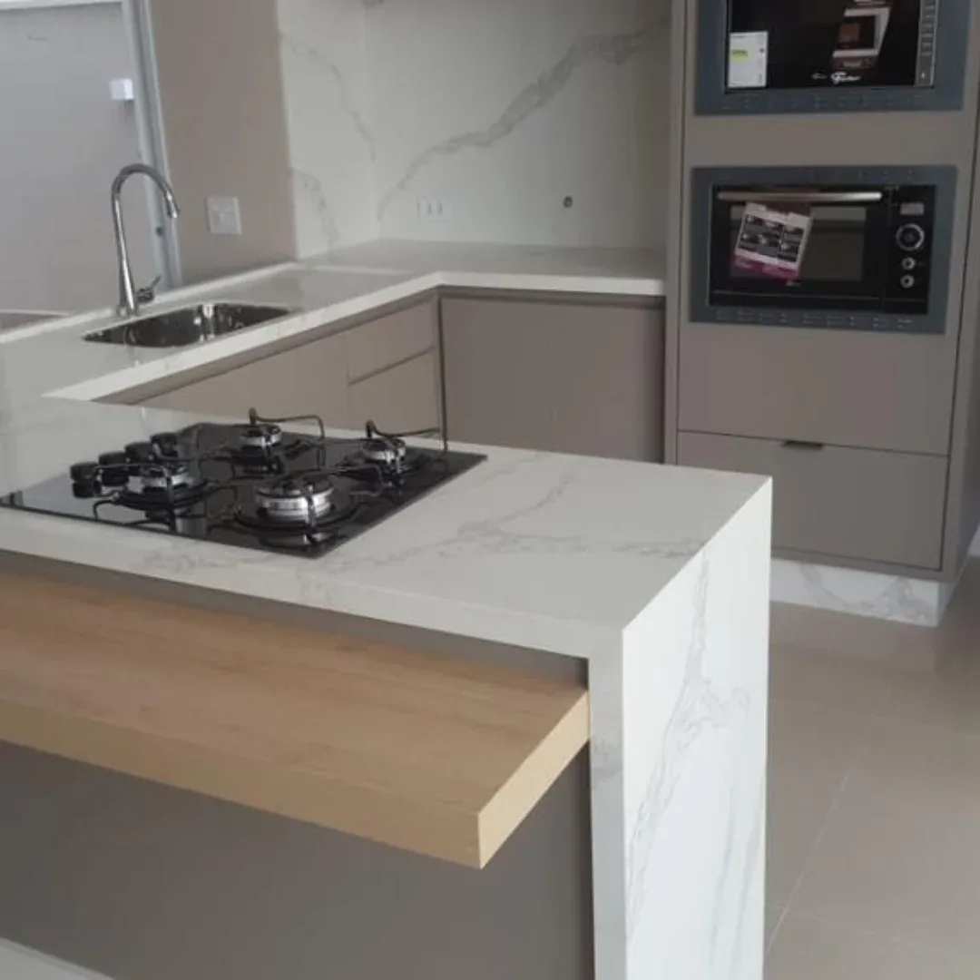 Cozinha com bancada branca de veios, cooktop e prolongamento de madeira